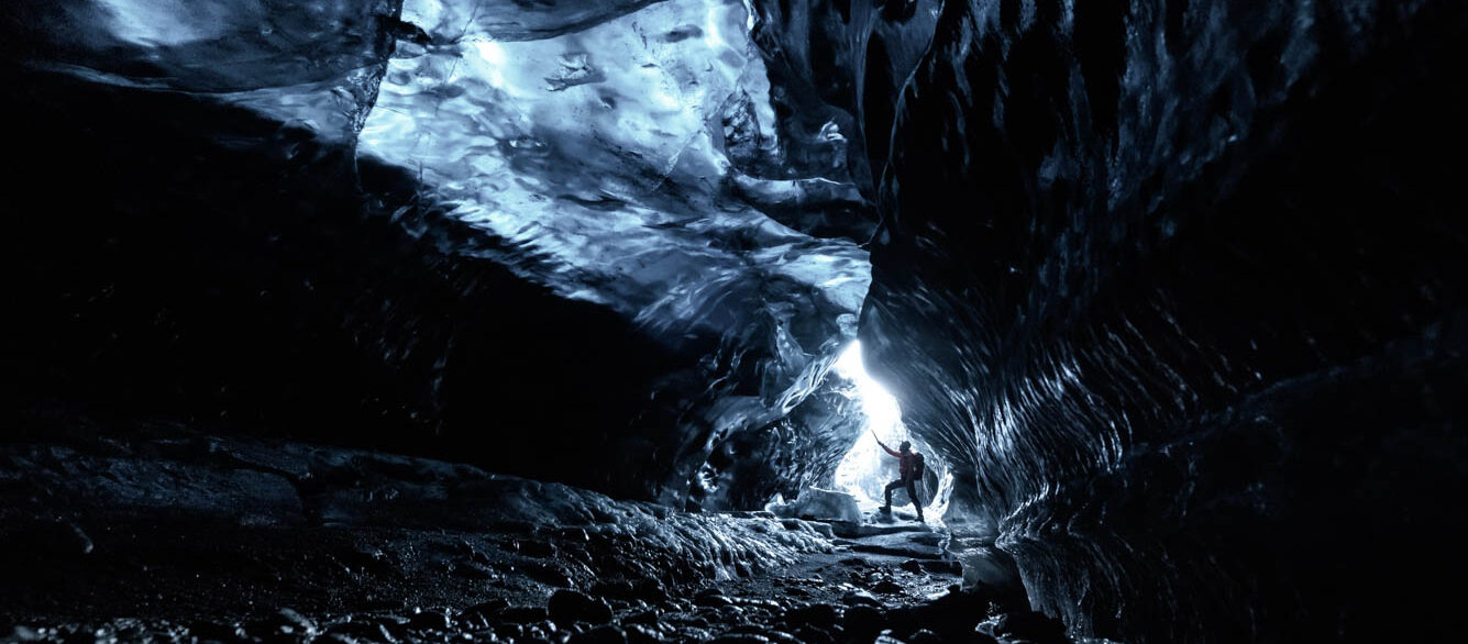 Explorer of the Ice cave Man in distance exploring cave made of ice