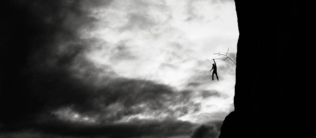 Defying the danger of life Man holding onto branch sticking out of rock wall