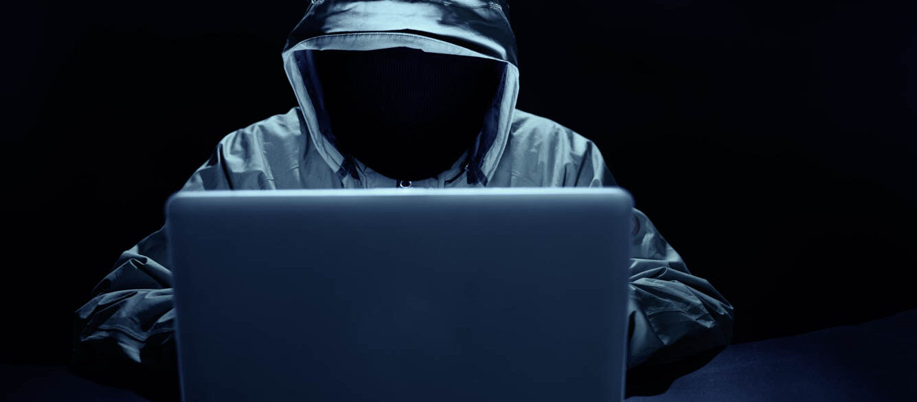 Hooded hacker attacking websites on laptop Hooded hacker attacking websites on laptop