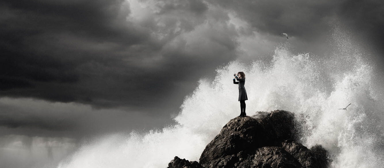 Waves breaking on rock where woman is standing looking through binoculars Waves breaking on rock where woman is standing looking through binoculars