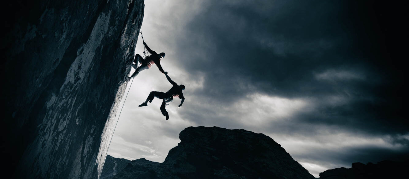Strength and success in the mountains Man climbing rock wall holding onto another climber