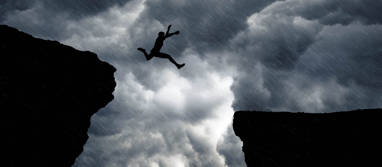 Low Angle View Of Man Jumping From Cliff Against Cloudy Sky Low Angle View Of Man Jumping From Cliff Against Cloudy Sky