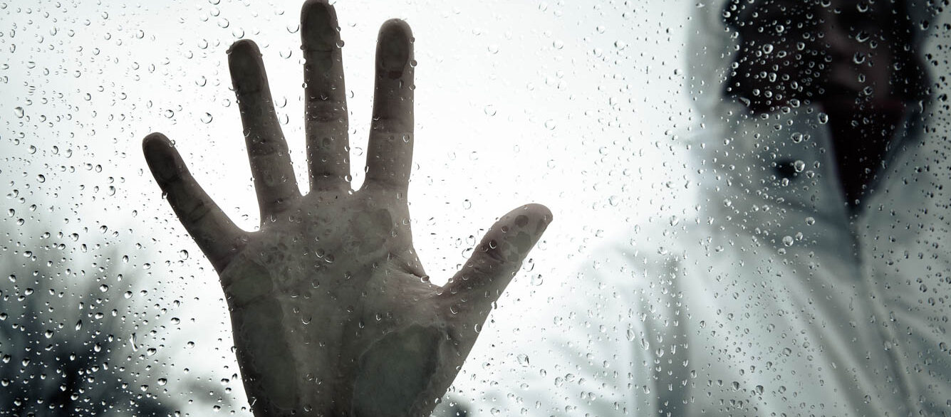 Hooded man placing hand on glass with water droplets Hooded man placing hand on glass with water droplets