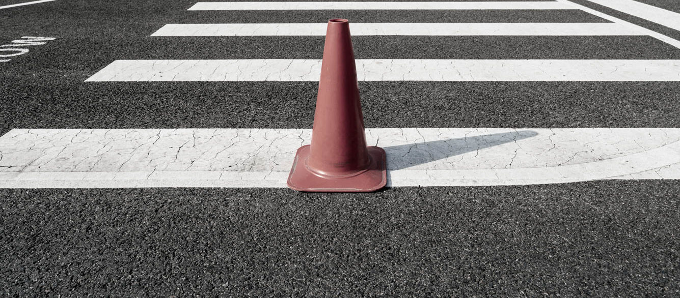 Single orange traffic cone on asphalt crosswalk Single orange traffic cone on asphalt crosswalk