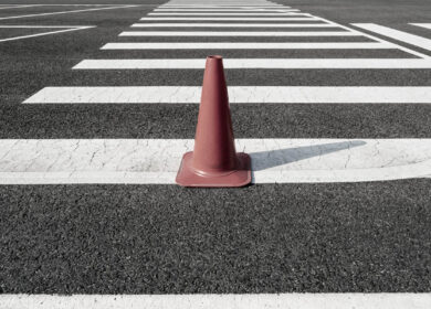 Single orange traffic cone on asphalt crosswalk Single orange traffic cone on asphalt crosswalk