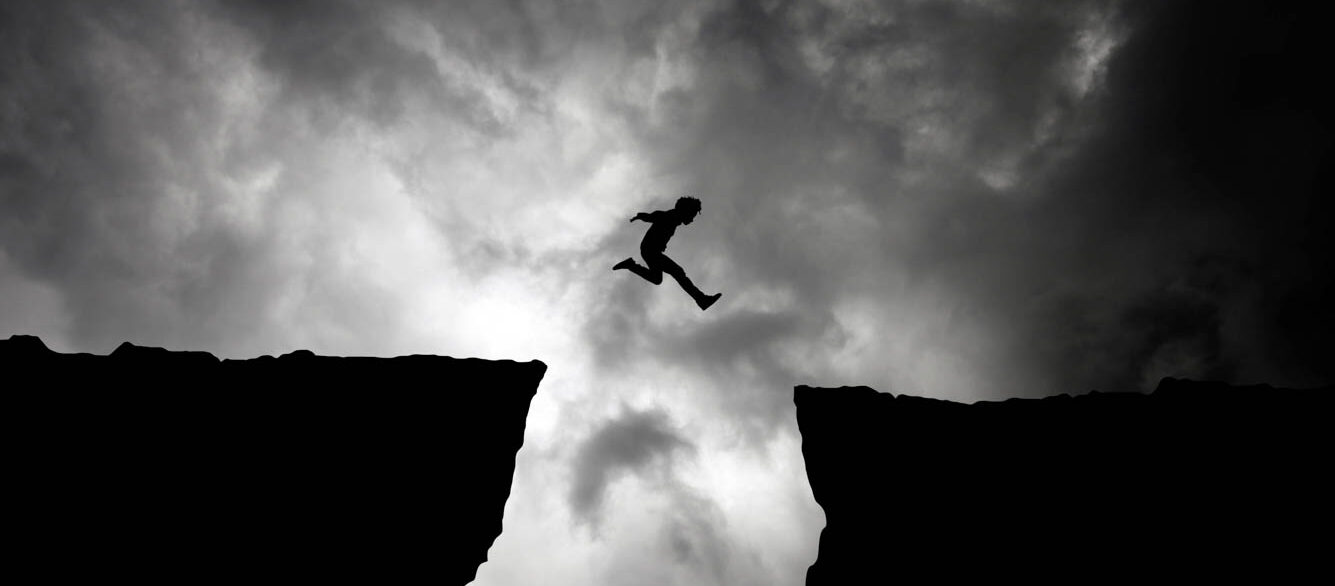 Silhouette Man Jumping Over Cliffs Against Cloudy Sky Silhouette Man Jumping Over Cliffs Against Cloudy Sky