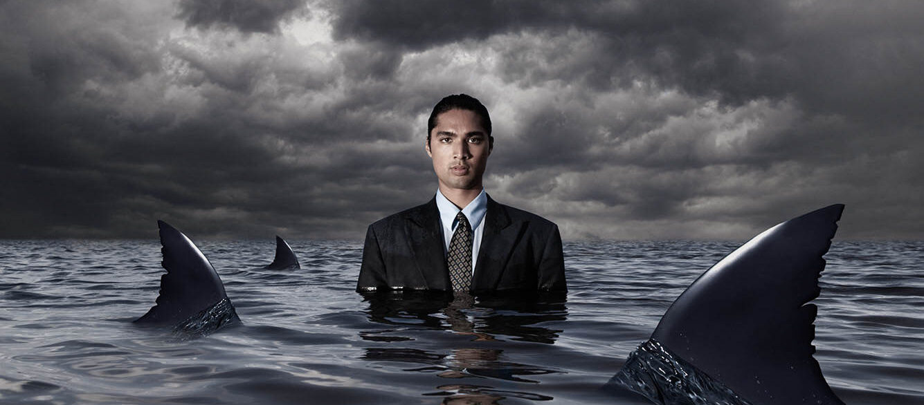 Hispanic businessman standing in water with sharks Hispanic businessman standing in water with sharks